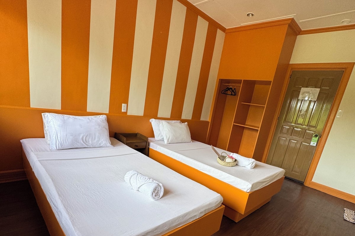 A hotel room with two beds, wooden flooring, and a striped wall design.