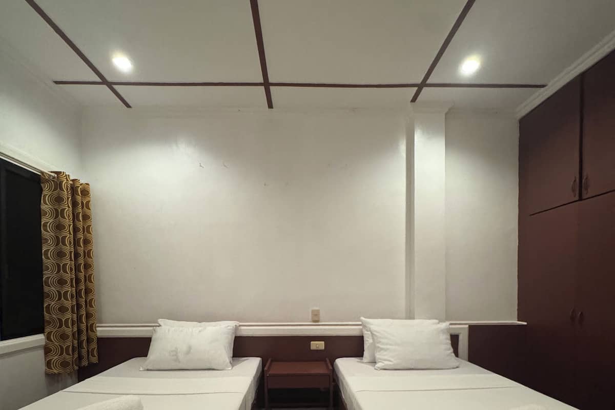 A hotel room with two single beds, a wooden floor, a window with curtains, and a wardrobe.