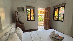 Une chambre d’hôtel avec un lit, des oreillers, une table de chevet, une lampe et deux fenêtres.