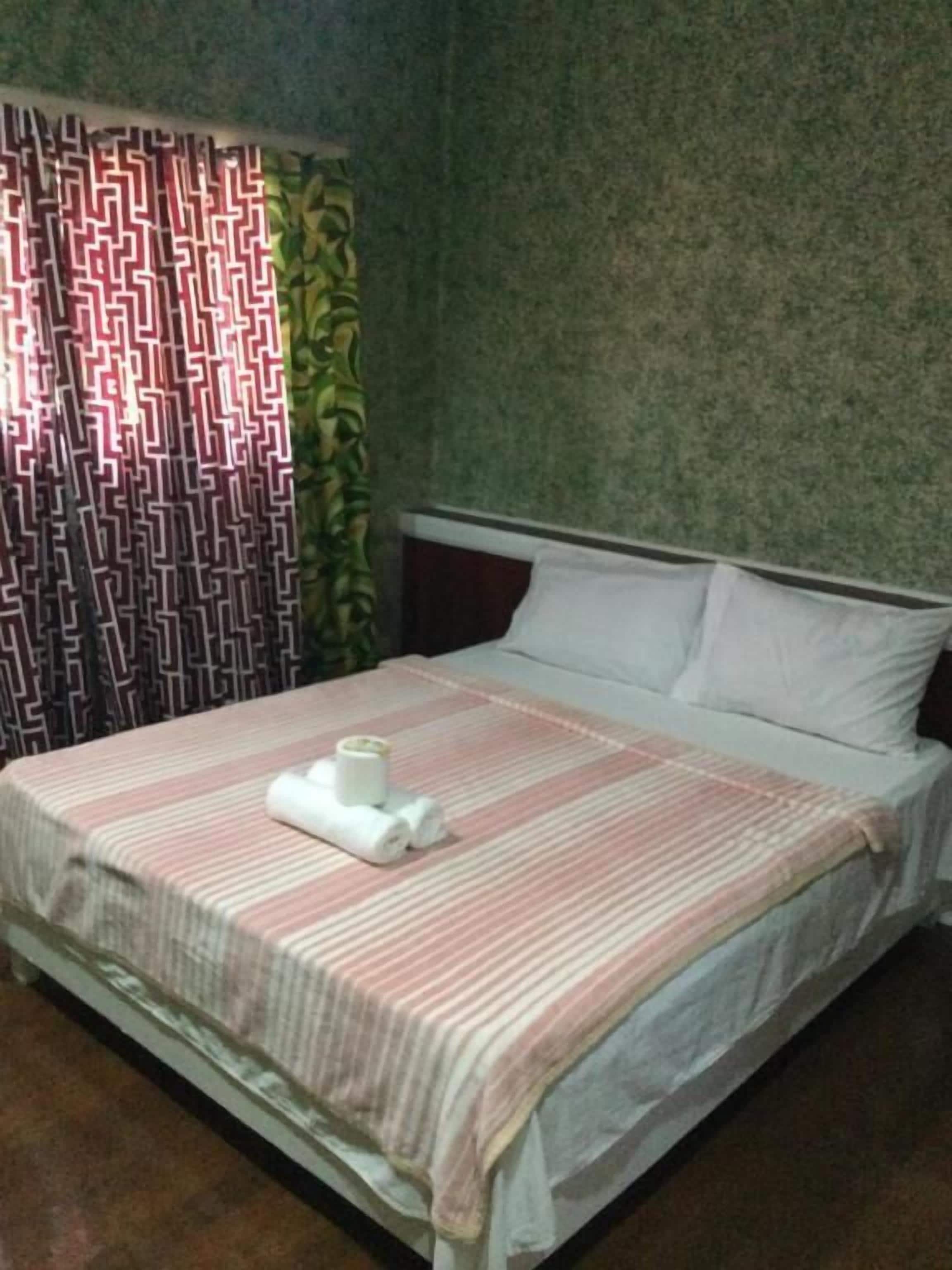 A neatly made bed with a striped bedspread and rolled towels, a patterned curtain, and a textured wall.