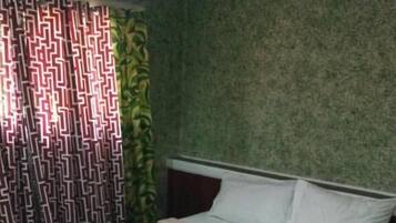 A neatly made bed with a striped bedspread and rolled towels, a patterned curtain, and a textured wall.