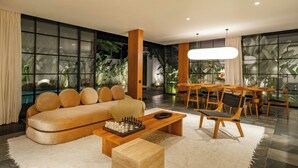 A modern living room with a sofa, a coffee table with a chess set, wooden chairs, and a dining area with a table and chairs. - Casa Siella (Kerobokan)