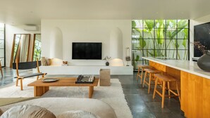 A modern living room with a flat-screen TV, a wooden coffee table, a sofa, and a bar area with stools. - Casa Siella (Kerobokan)