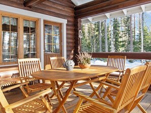 Une terrasse en bois avec une table ronde et des chaises, de grandes fenêtres et une vue sur les arbres.