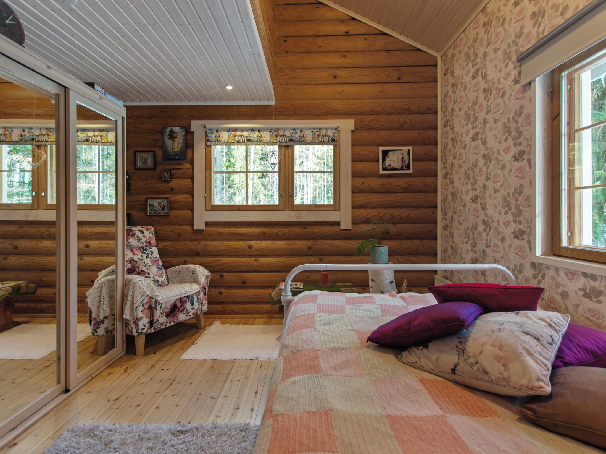 A log cabin interior with a bed, a chair, a window, and a mirror.