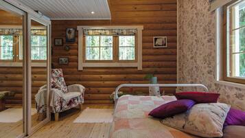 A log cabin interior with a bed, a chair, a window, and a mirror.