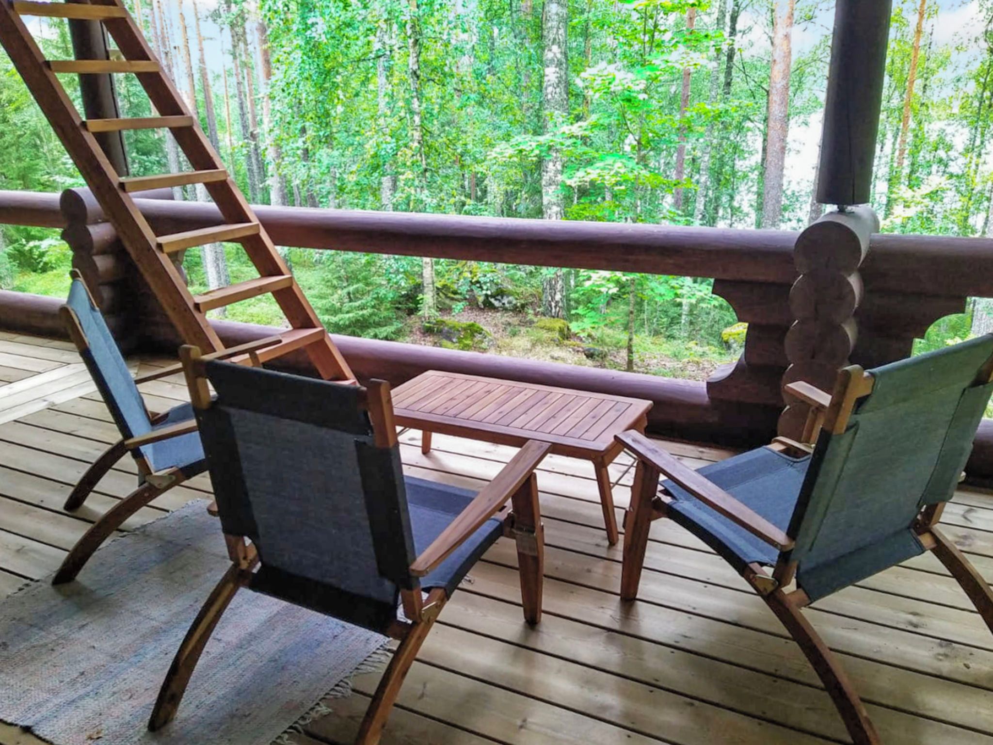 A wooden deck with a table and two chairs, overlooking a forested area.