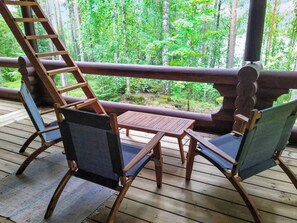 A wooden deck with a table and two chairs, overlooking a forested area.