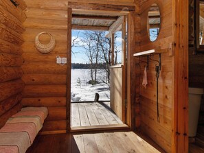 L’intérieur d’un chalet en bois, avec un banc, un panier en osier et une vue sur un paysage enneigé.