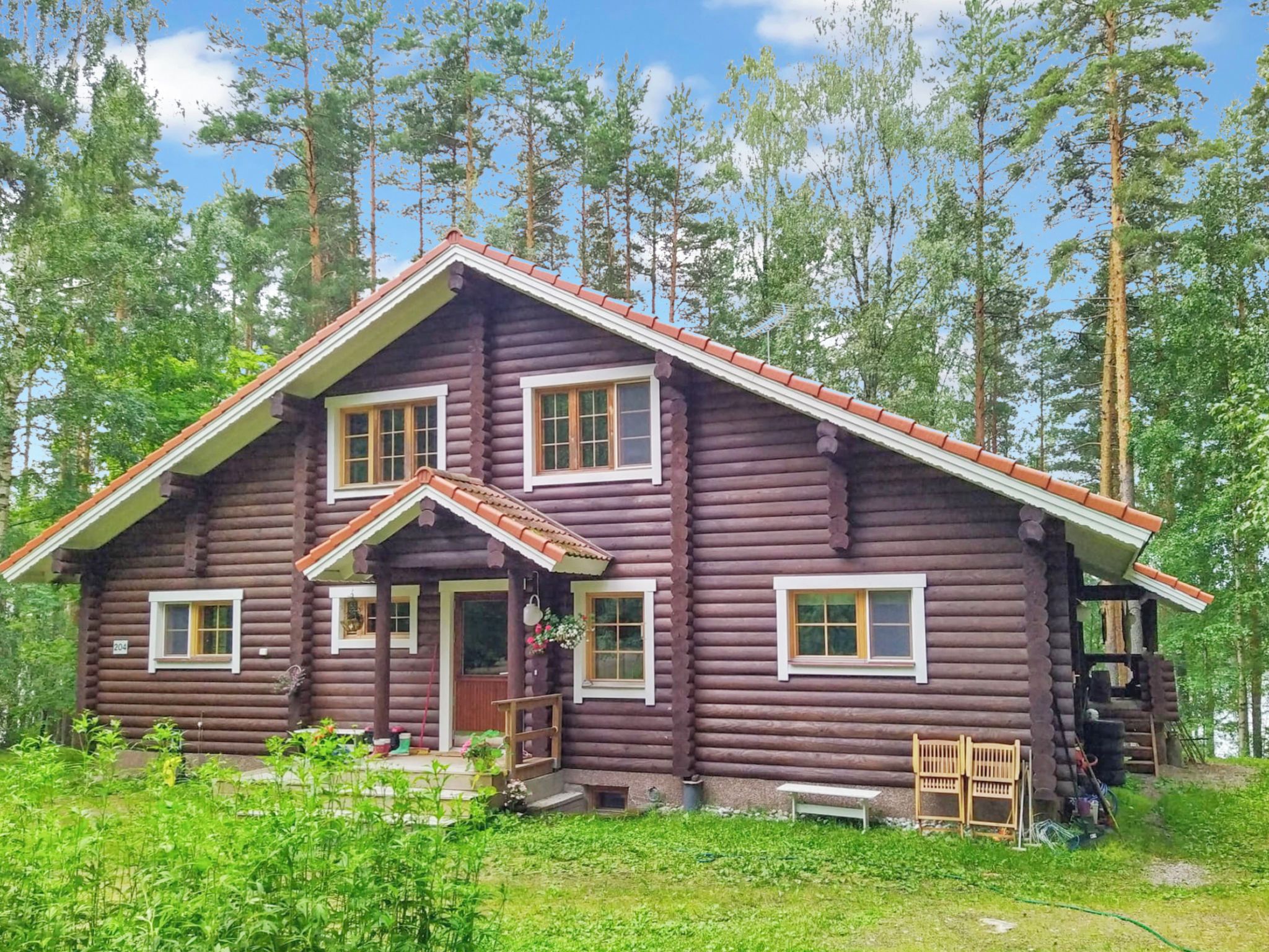 Hirsimökki, jossa on harjakatto, useita ikkunoita ja kuisti, jossa on penkki.