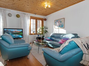 Ett vardagsrum med två blå lädersoffor, ett soffbord i glas, en tv och ett fönster med gardiner.