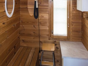 A wooden interior with a small stool, a white bench, a door with a window, and a white circular object on the wall.
