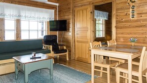 Un acogedor interior de cabaña con detalles de madera, un sofá, una mesa de comedor con sillas, un televisor y un ventanal con cortinas.