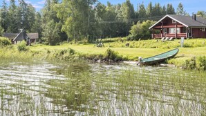 Una cabaña junto al lago con un muelle, rodeada de exuberante vegetación y árboles.