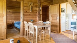 Interior de una cabaña de madera con comedor, una cocina con electrodomésticos blancos y techo de madera.