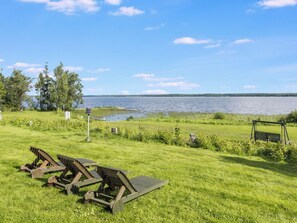 Une zone herbeuse avec des bancs en bois et une aire de jeux avec des balançoires, le tout surplombant un lac.
