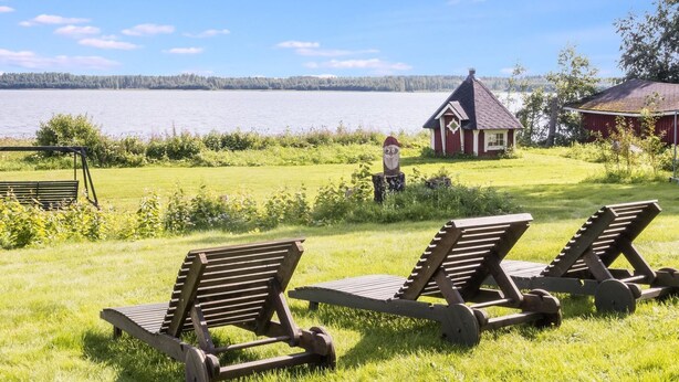 Un entorno junto al lago con sillones de madera y una cabaña pequeña roja.
