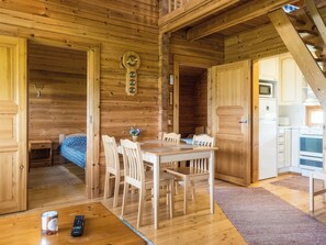 A wooden interior with a dining table, chairs, a bed, and a kitchen area.