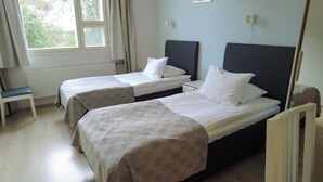 A room with two single beds, a chair, a radiator, and a window with curtains. - Budget Double or Twin Room - Lapin Satu Hotel (Lapland)