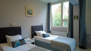 Habitación de hotel con dos camas, una mesita de noche, un cuadro en la pared y una ventana con cortinas.
