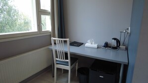 Un espacio de oficina pequeño y ordenado, con una silla blanca, un escritorio con una computadora, una caja de pañuelos, una cafetera y un cesto de basura.