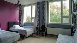 Een kamer met twee eenpersoonsbedden, een stoel, een radiator en een raam met gordijnen.