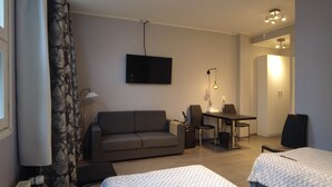 A hotel room with a sofa, a desk with two chairs, a TV mounted on the wall, and a bed with a white cover. - Superior Double or Twin Room with Terrace - Lapin Satu Hotel (Lapland)