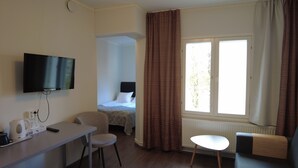 Une chambre d’hôtel avec un lit, un bureau et une chaise, une télévision et une fenêtre avec des rideaux.