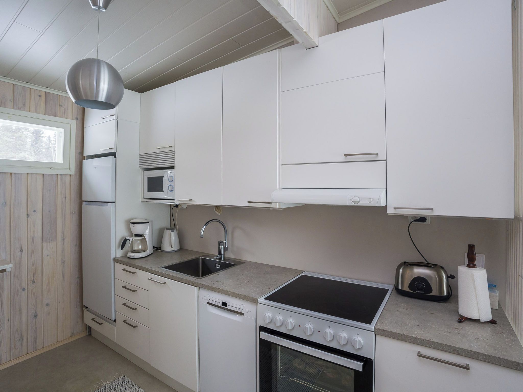 Ett kompakt kök med vita skåp, en inbyggd mikrovågsugn, en kaffebryggare, en brödrost och en diskmaskin.