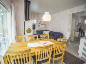 A modern interior with a dining area featuring a wooden table and chairs, a black stove, and a grey sofa in the background.
