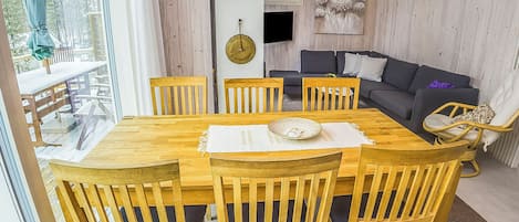 A wooden dining table with six chairs, a sofa, and a hanging light fixture in a room with wooden walls.