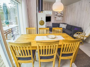 A wooden dining table with six chairs, a sofa, and a hanging light fixture in a room with wooden walls.