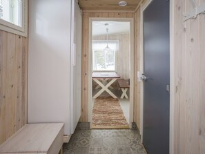 Ein schmaler Korridor mit Holzwänden, einer Bank, einem Tisch mit weißem X-förmigen Gestell und einem gemusterten Teppich.