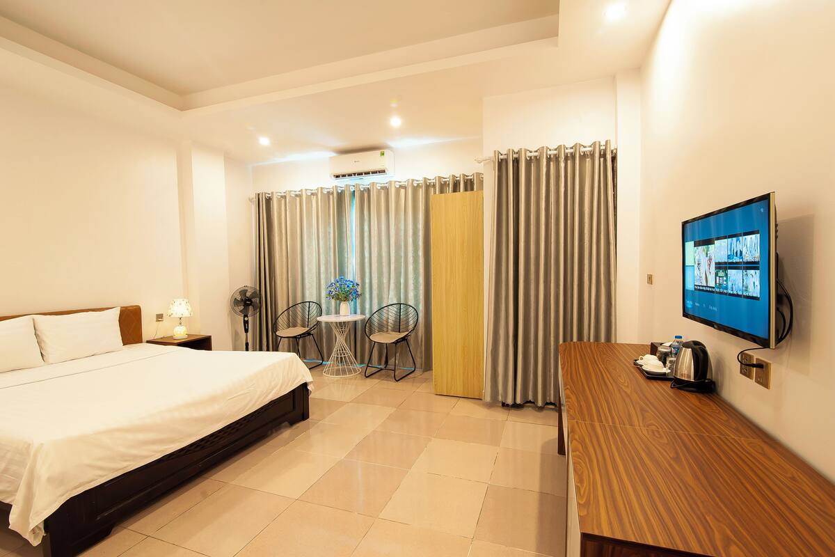A hotel room with a bed, a desk, a TV, a fan, and a small table with chairs.