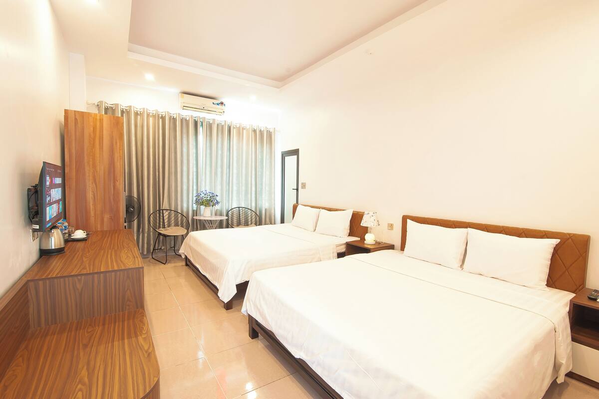 A hotel room with two beds, a wooden desk, a small table with a chair, and a TV.