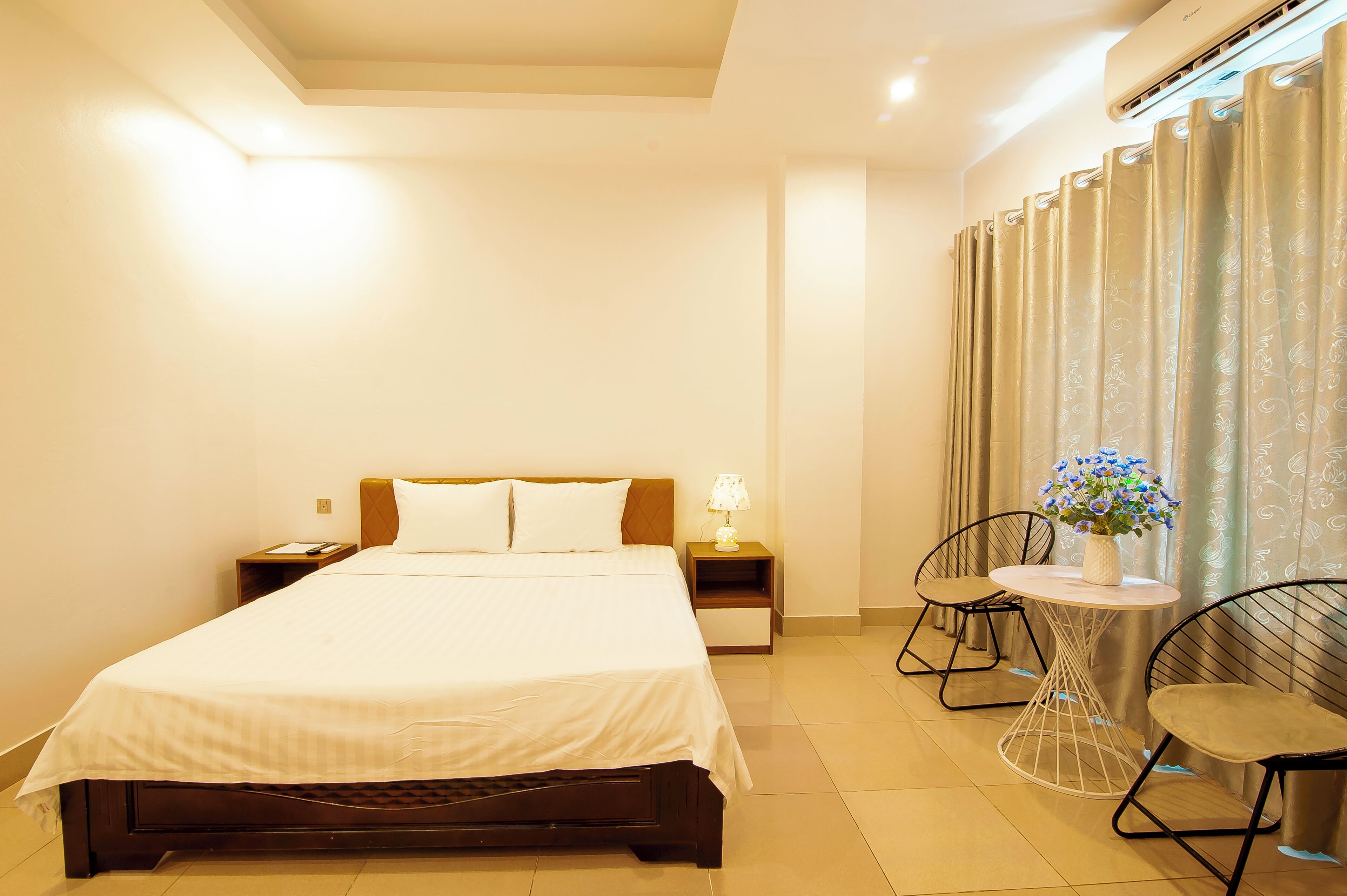 A hotel room with a bed, bedside tables, a lamp, a chair, and a small table with a vase of flowers.