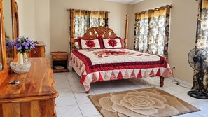 A bedroom with a wooden bed, floral curtains, a bedside table with a vase, and a floor rug.