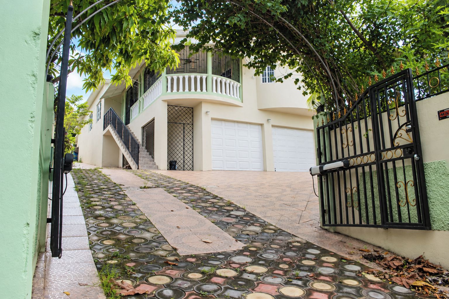 Um edifício residencial com entrada por portão, escadaria que leva a uma varanda e entrada pavimentada.