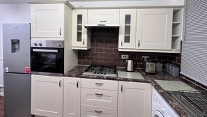 A compact kitchen with white cabinets, a built-in oven, a gas stove, a refrigerator, and a washing machine.