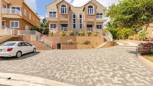 A multi-story residential building with a paved driveway, balconies, and a car parked in front. - Luxury Sea-View Townhouse, Pool , Ocho Rios (Ocho Rios)