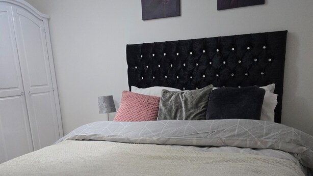 A neatly made bed with a tufted headboard, a white wall, and two framed pictures above it. - Emerald Apartment Sleeps 4 with Parking (London)