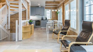 Un interior moderno con una escalera de madera, una cocina y un comedor con sillas de cuero.