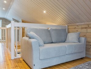 Un canapé gris clair avec des coussins, dans une pièce dotée d’un plancher en bois et d’un plafond en pente.