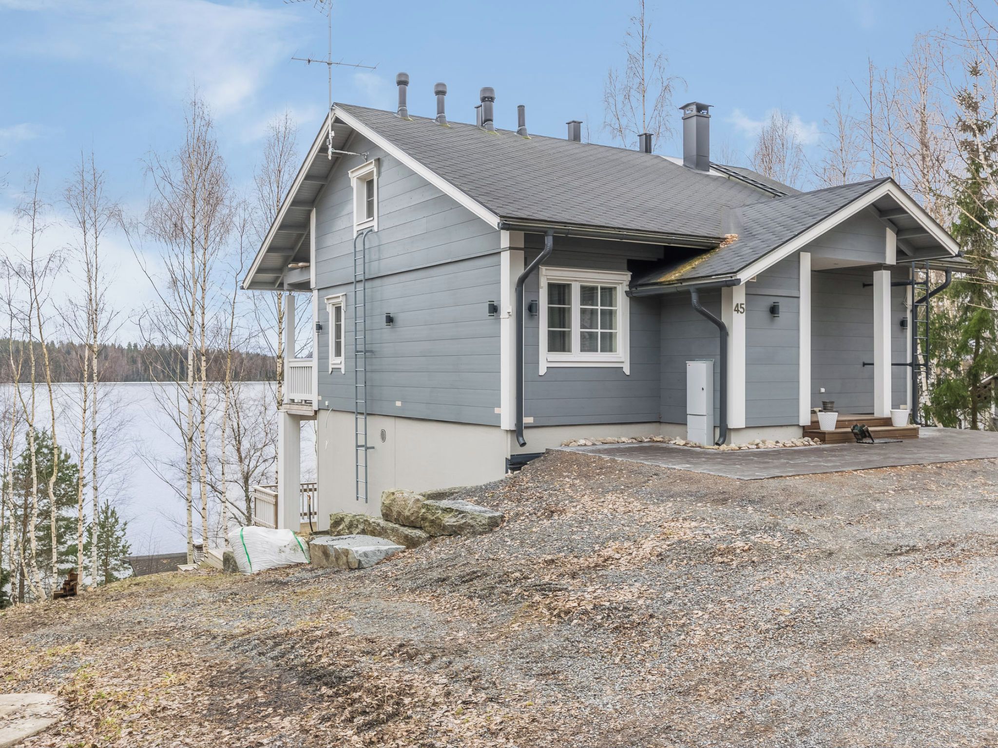 A two-story house with a grey exterior, a chimney, and a dock extending into a lake.