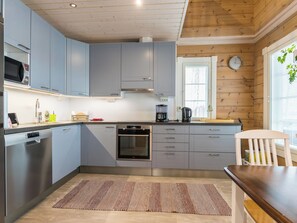 Une cuisine moderne avec des meubles gris, un four encastré, une machine à café et un plafond en bois.