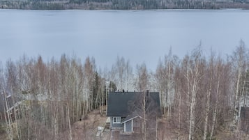 A house with a dark roof, surrounded by leafless trees, near a large body of water.