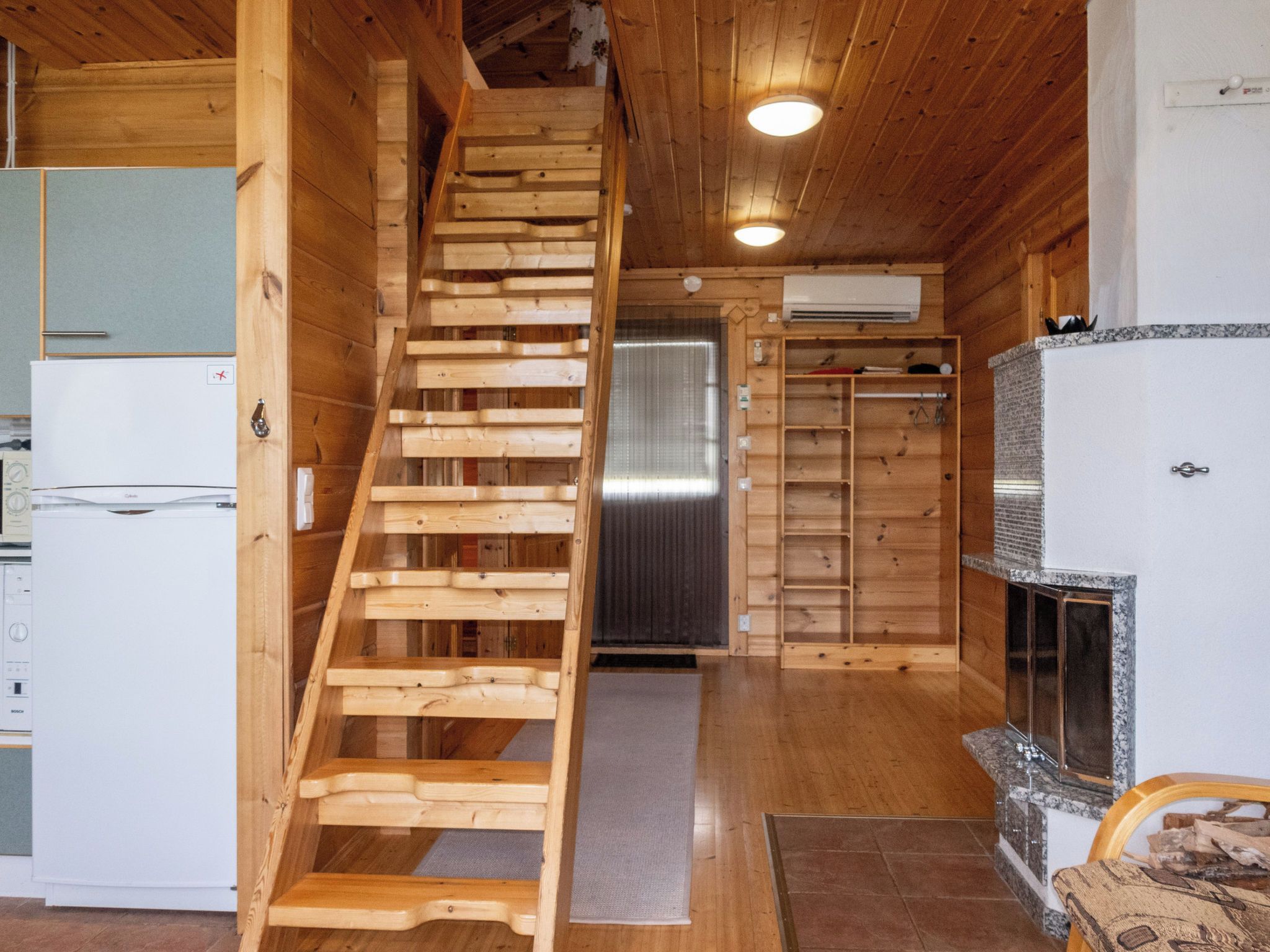 Un interior de madera con una escalera de madera, una zona de cocina con refrigerador y una chimenea.