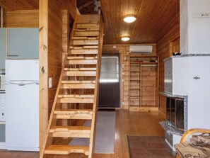 A wooden interior with a wooden staircase, a kitchen area with a refrigerator, and a fireplace.