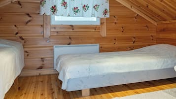 Ein kleiner, gemütlicher Raum mit Holzwänden und schrägen Decken, ausgestattet mit zwei Einzelbetten und einem Fenster mit einem Blumenvorhang.