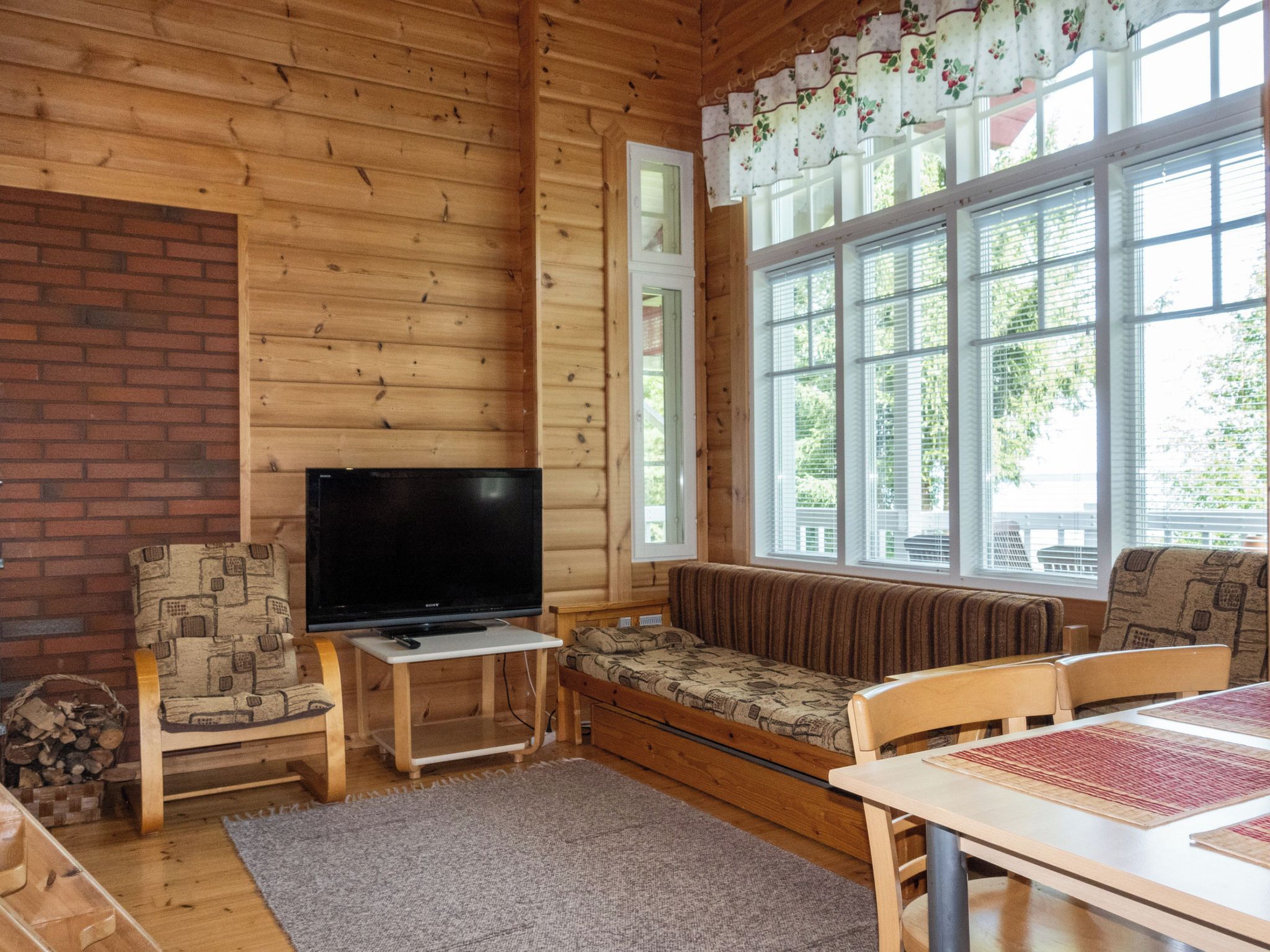 Ein gemütliches Blockhäuschen-Interieur mit Fernseher, Sitzecke und großen Fenstern.